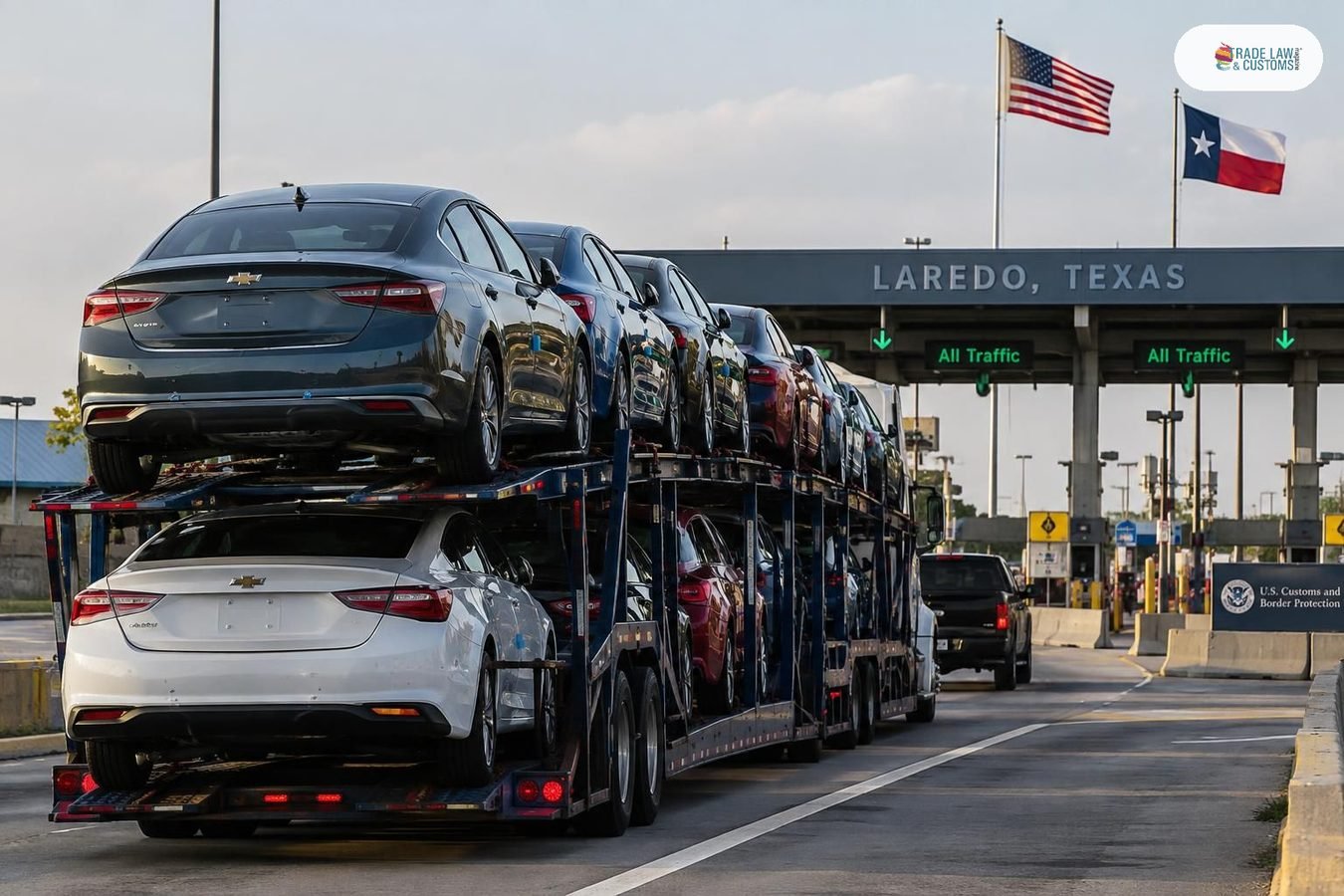 Camión transportador de vehículos nuevos cruzando la frontera México-EE.UU. en un punto de inspección aduanera.